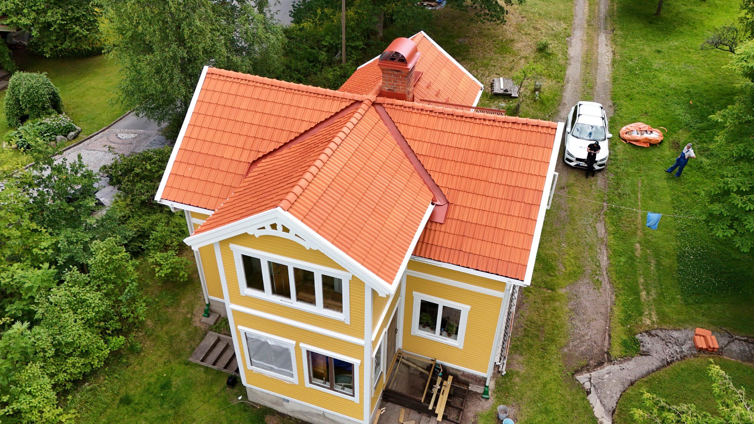 Ett gult villahus med sluttande, orange tegeltak. Taket har en takstege och skorsten.