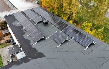 Fågelvy ovanför ett radhus med solceller och papptak. I bakgrunden syns tomten samt några träd.