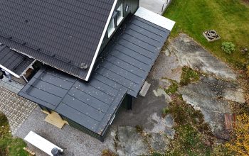 Ett villahus med sluttande hustak gjort av betongpannor och bandtäckt plåttak. På taket finns snörasskydd och takstege.