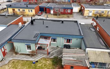 Fågelvy över ett grönt kedjehus efter takomläggning med asfaltpapp. Runt huset ligger grannhus.