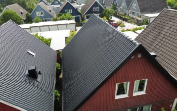 Ett rött hus med tak av sluttande betongpannor. I bakgrunden syns likande hus i andra färger.